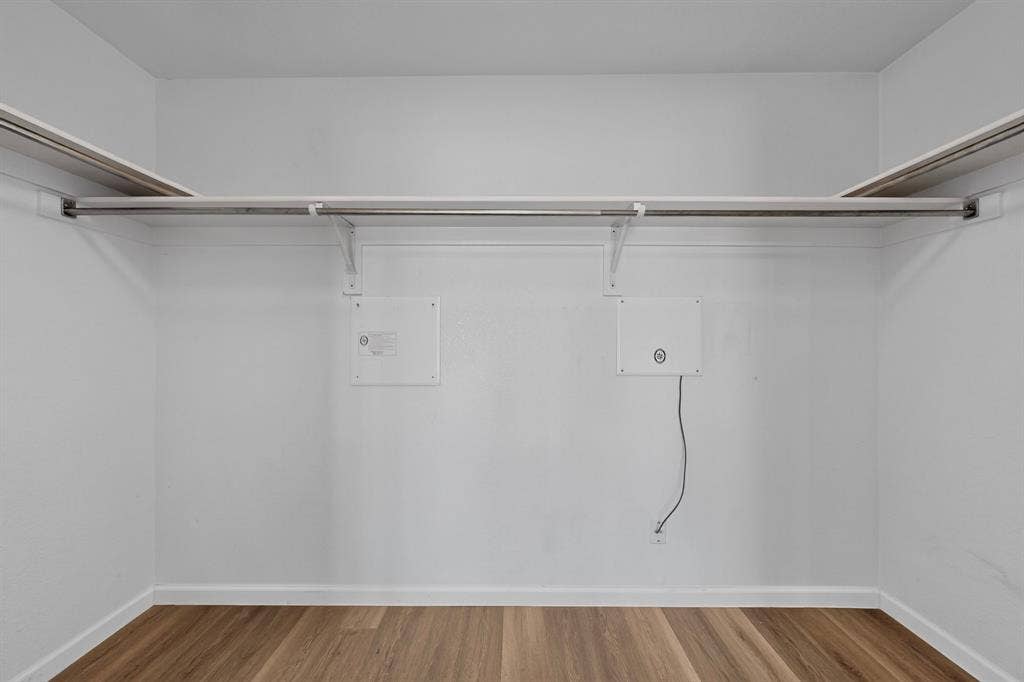 Closet featuring wood-finish flooring, white walls, and built-in shelving with hanging rods