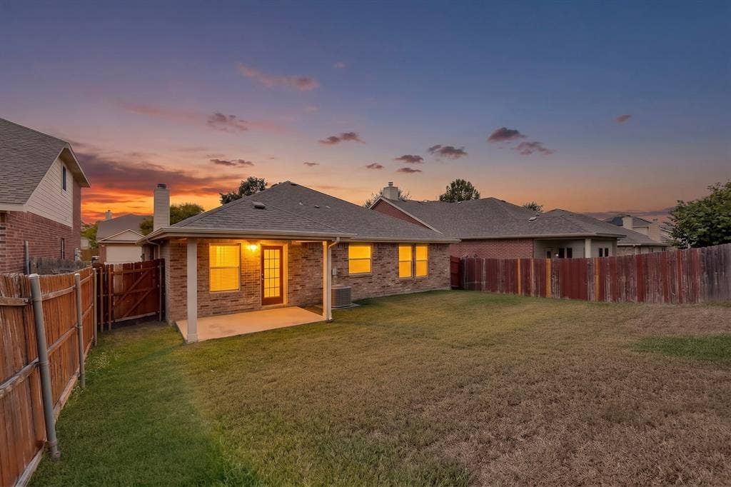 Expansive backyard featuring a covered concrete patio, brick exterior, and a wood privacy fence