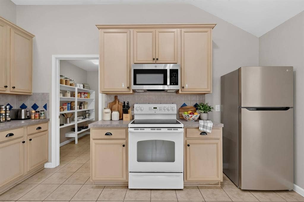 Kitchen featuring light-toned cabinetry, stainless steel microwave, white electric range, and a stainless steel refrigerator