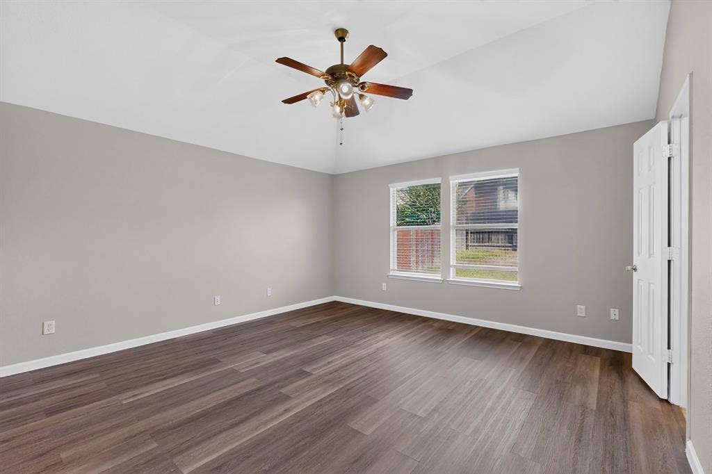 Spacious room featuring wood-finish flooring, two windows, and a ceiling fan with integrated lighting