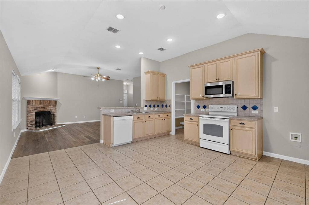 Open-concept kitchen featuring tile flooring, wood-finish cabinetry, a stainless steel microwave, and white appliances