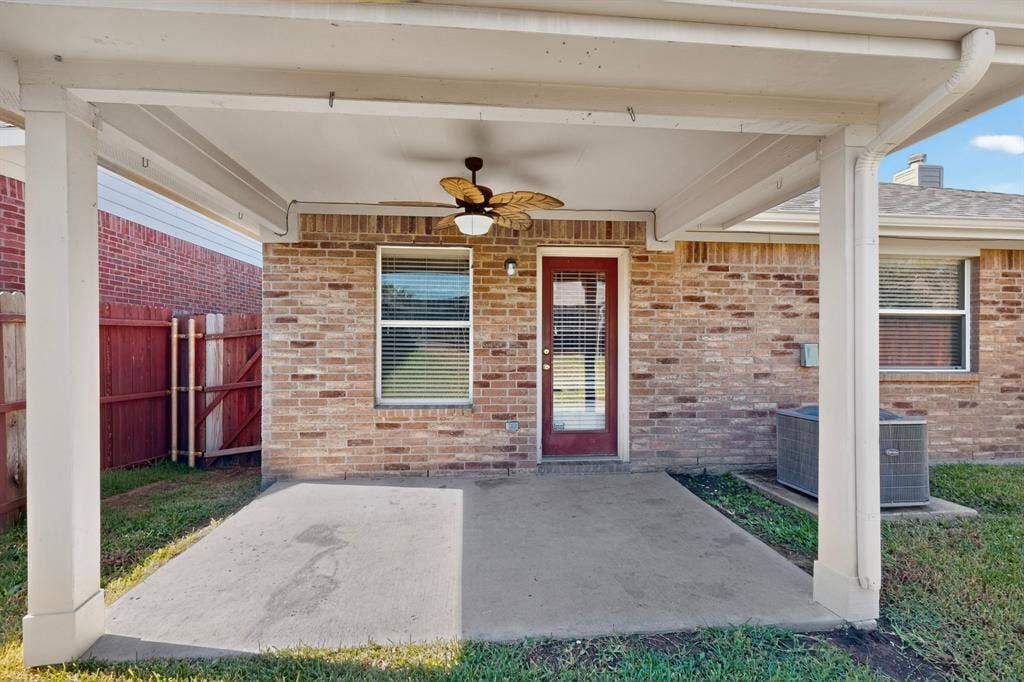 Covered patio with a ceiling fan, brick exterior, and a red-painted glass-paneled door