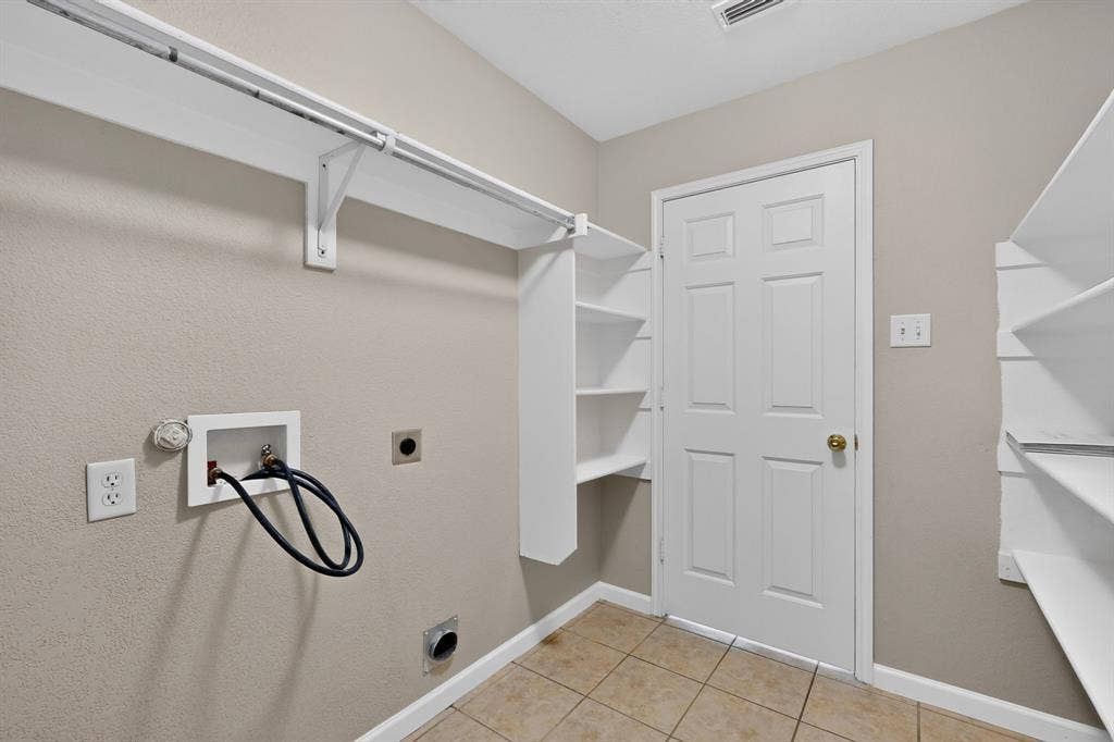 Dedicated laundry area featuring tile flooring, built-in shelving, and a hanging rod