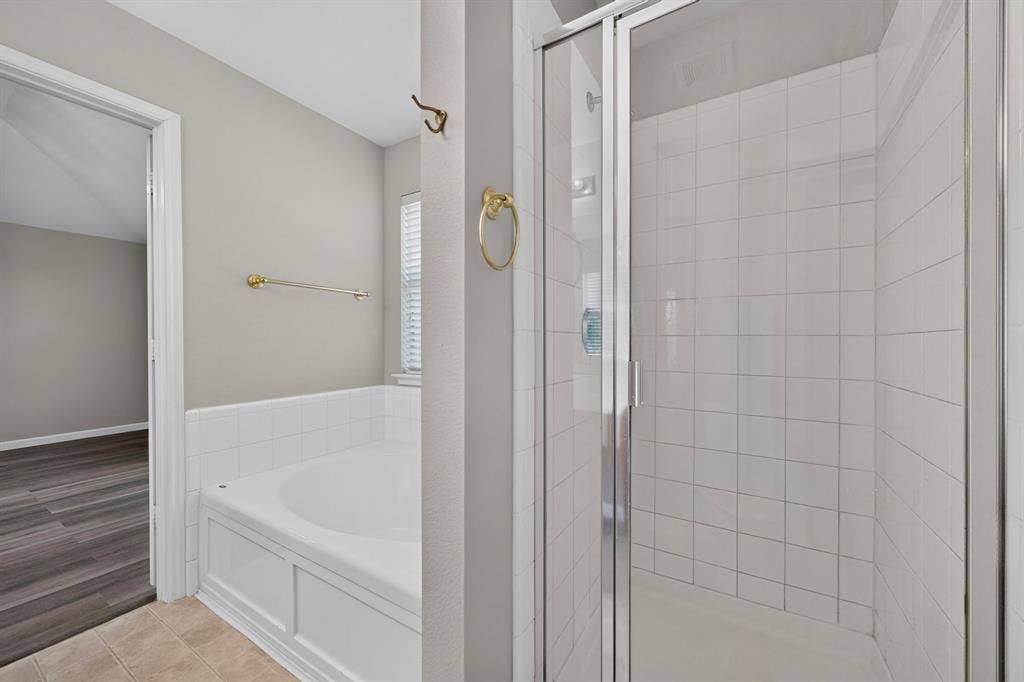 White tiled shower enclosure with clear glass door, alongside a built-in soaking tub with white tile surround