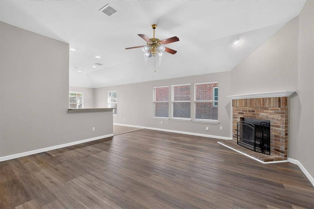 Vaulted ceilings featuring recessed lighting, wood-finish flooring, a brick fireplace with a white mantel, a ceiling fan with integrated lighting, and multiple windows