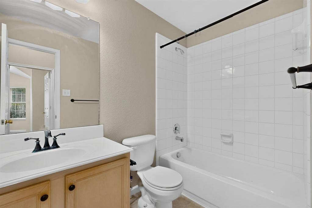 Bathroom featuring a built-in vanity with a white countertop and integrated sink, a commode, a shower/tub combination with white subway tile surround, and a wall-mounted mirror