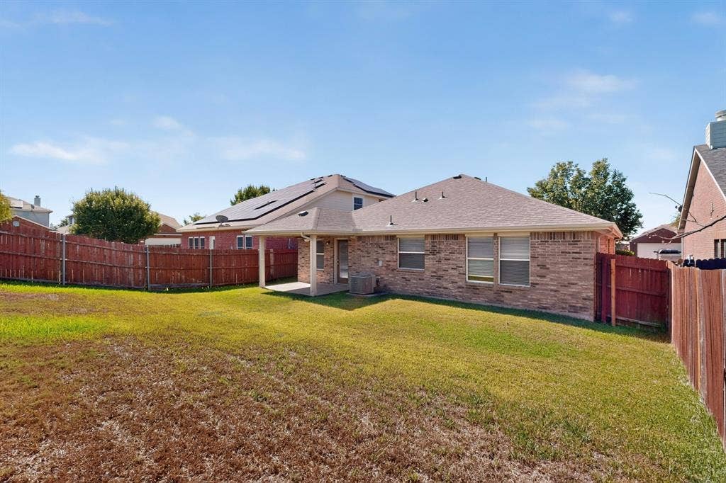 Expansive backyard featuring a wood privacy fence, brick exterior, covered patio, and multi-pane windows