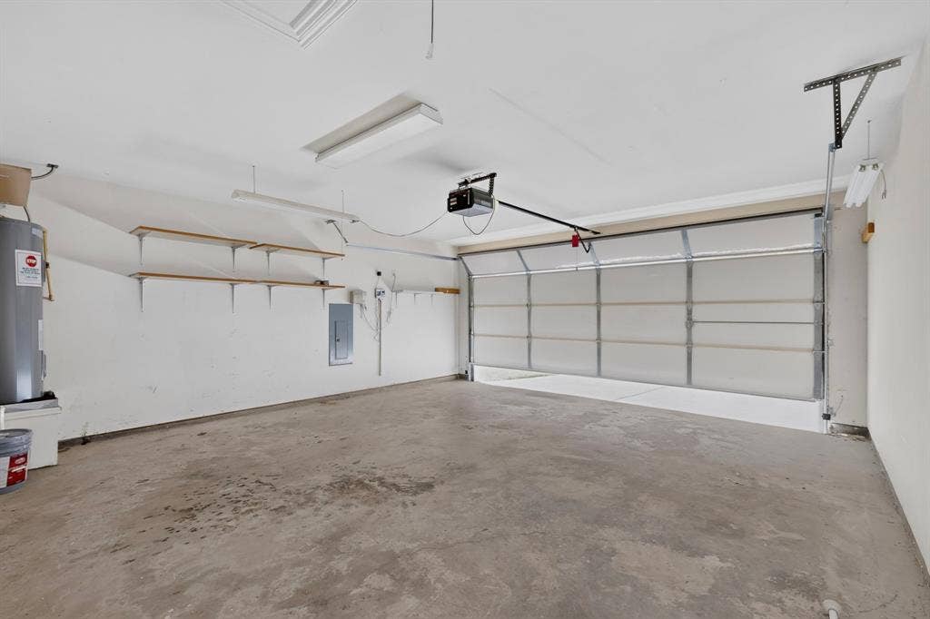 Concrete flooring with automatic garage door opener, overhead lighting, and built-in shelving