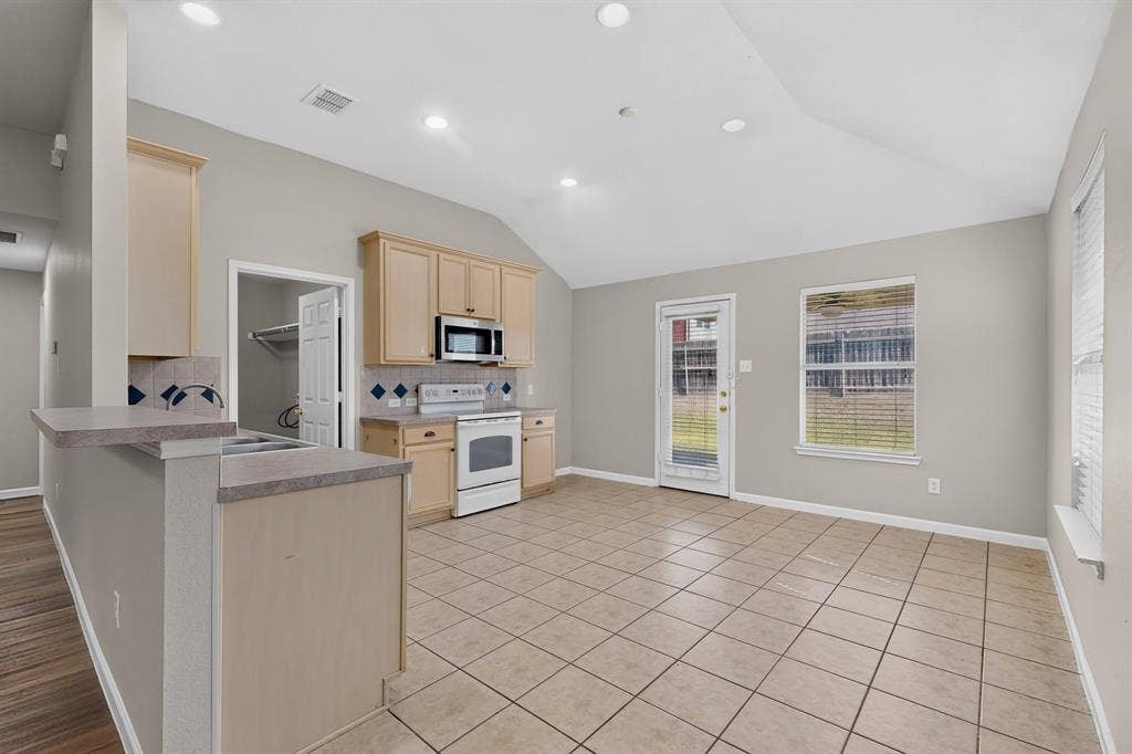 Kitchen and dining area featuring tile flooring, vaulted ceiling, recessed lighting, and a kitchen peninsula with countertop seating
