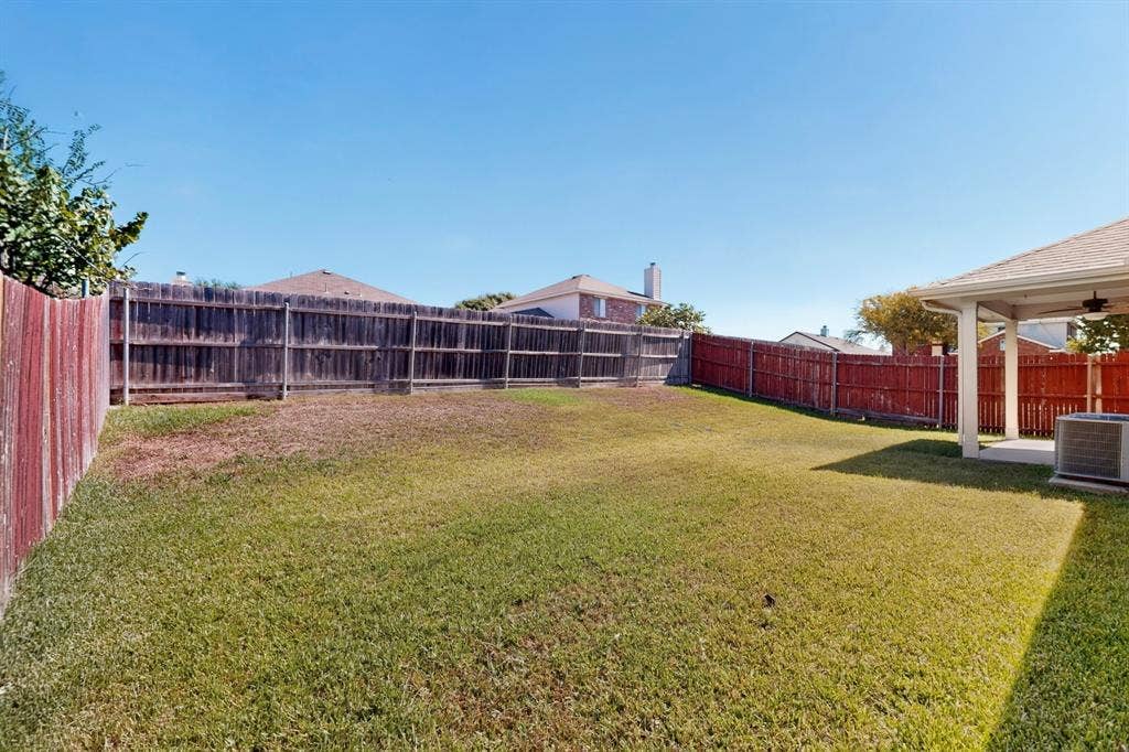 Expansive fenced backyard with a covered patio, ceiling fan, and concrete flooring