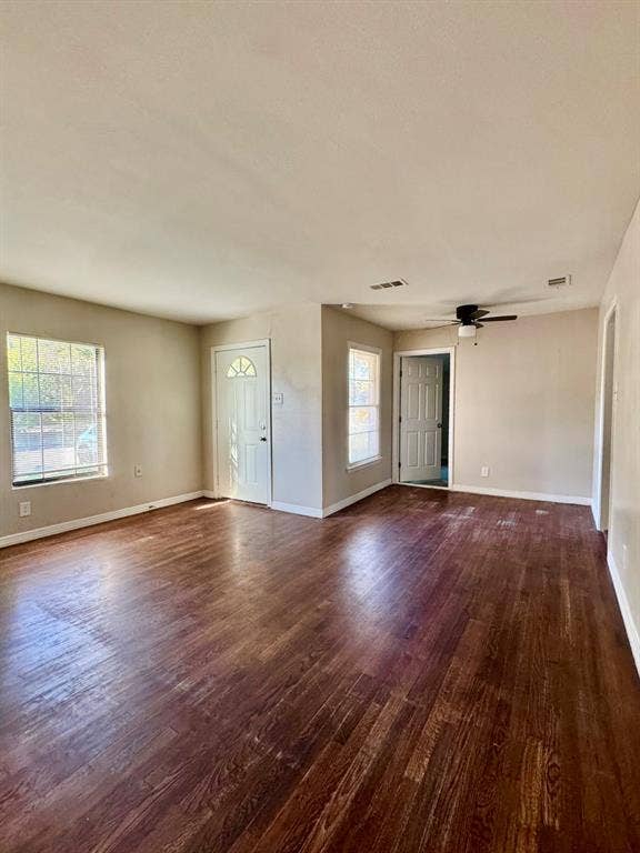 8018 S Reno Court, Dallas, TX 75217 Spacious room featuring wood-finish flooring, multiple windows, a ceiling fan, and two panel doors