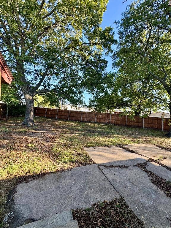 8018 S Reno Court, Dallas, TX 75217 Expansive rear yard featuring a wood privacy fence, mature trees, and concrete patio