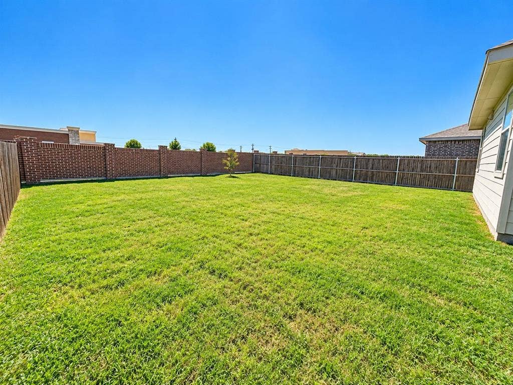 1605 River Crossing Drive, Anna, TX 75409 Expansive backyard featuring a large grass lawn, wood privacy fencing, and a brick privacy fence with stone accents