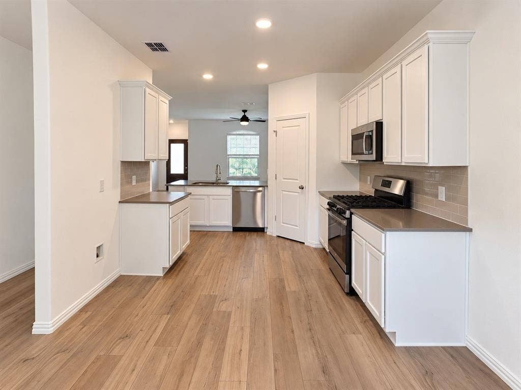 1605 River Crossing Drive, Anna, TX 75409 Kitchen featuring wood-finish flooring, recessed lighting, white cabinetry, integrated stainless steel appliances, and a subway tile backsplash