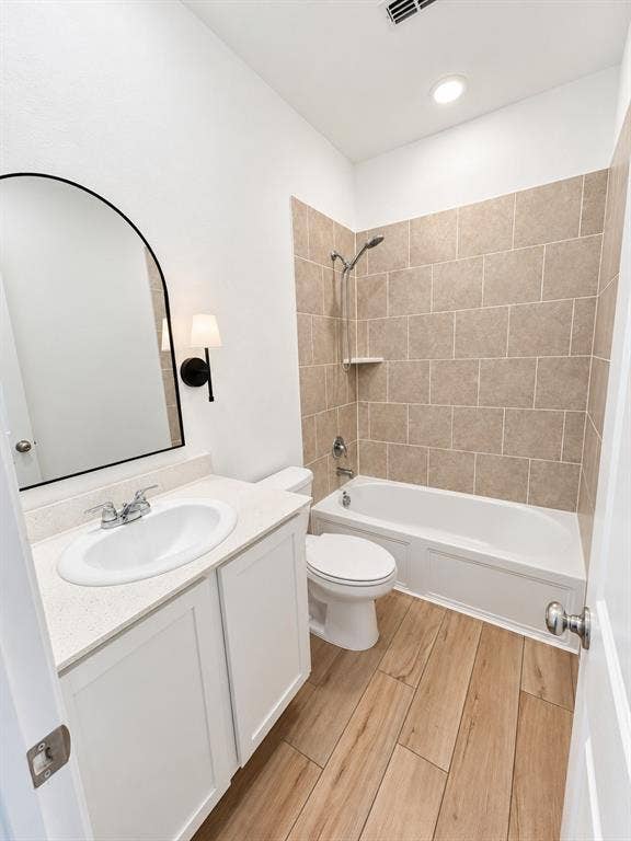 1605 River Crossing Drive, Anna, TX 75409 Wood-finish flooring, white vanity with integrated sink, chrome faucet, white bathtub with a tile surround, and a wall-mounted light fixture