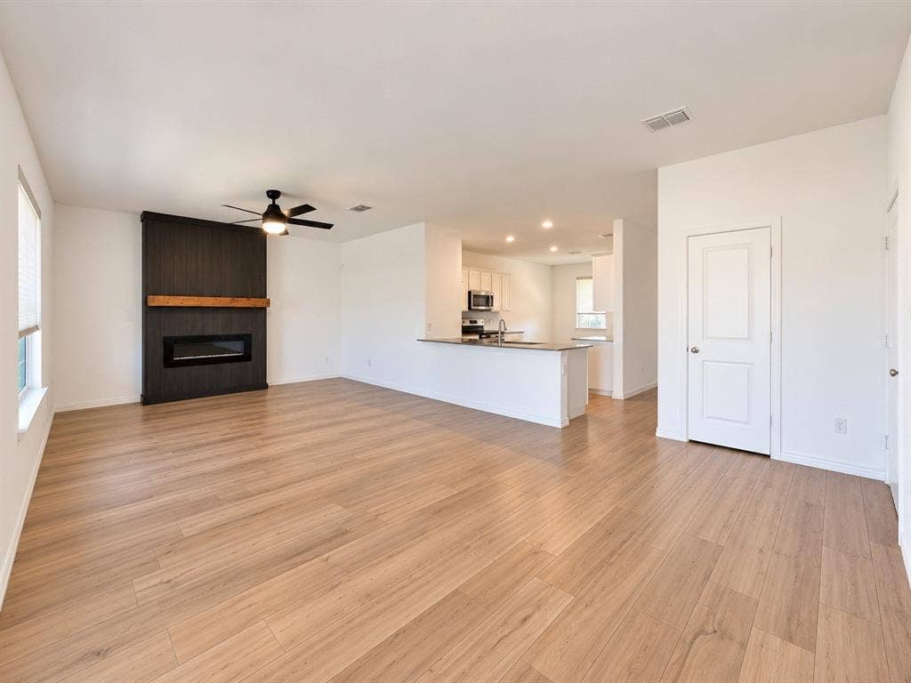 1605 River Crossing Drive, Anna, TX 75409 Spacious open-concept living area featuring wood-finish flooring, a modern fireplace with a dark wood-paneled surround and natural wood mantel, and a ceiling fan