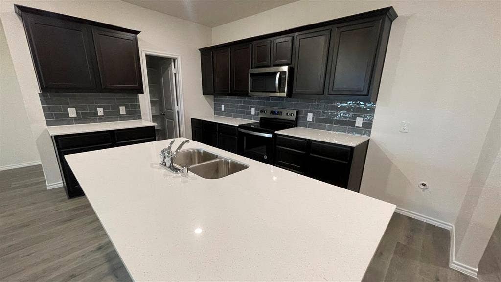 409 White Willow Drive, Nevada, TX 75173 Kitchen featuring dark wood-finish cabinetry, light-toned countertops, subway tile backsplash, stainless steel microwave, and wood-finish flooring