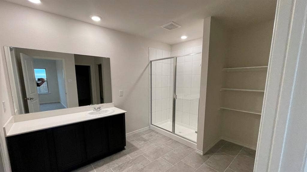 409 White Willow Drive, Nevada, TX 75173 Spacious bathroom featuring a glass-enclosed shower, a vanity with a single sink and dark cabinetry, and built-in shelving