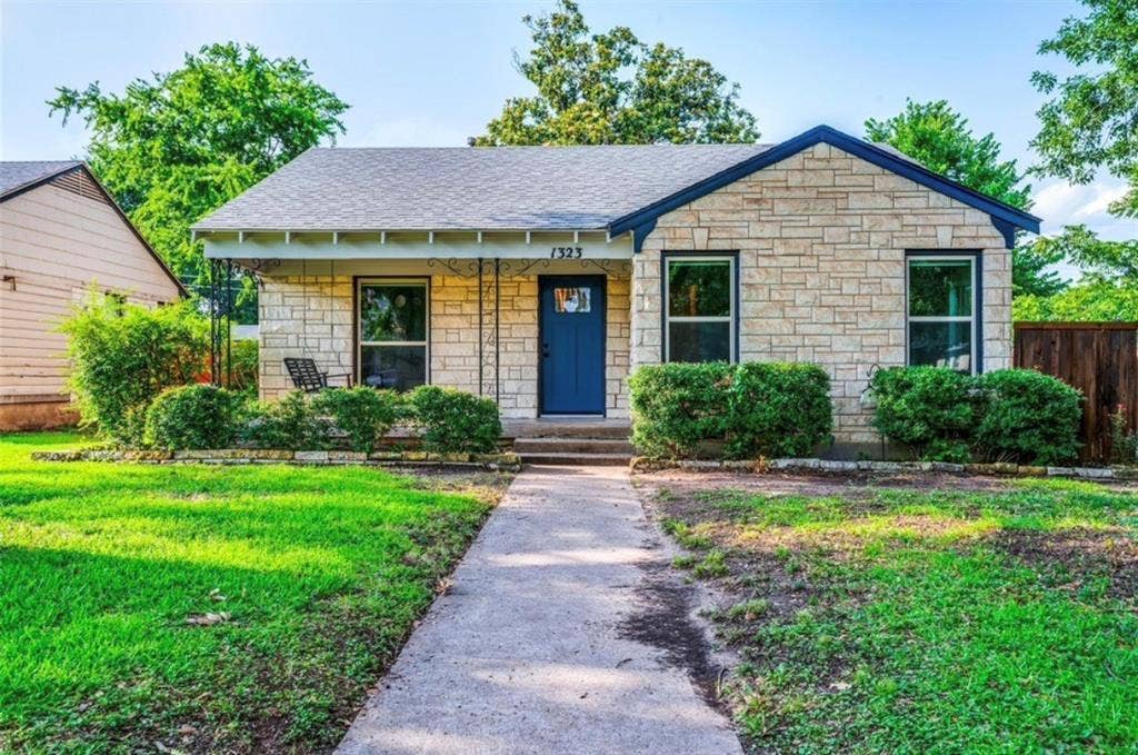 1323 Engle Avenue, Dallas, TX 75224 Stone exterior with a dark blue front door, covered porch with decorative iron columns, and landscaped front yard