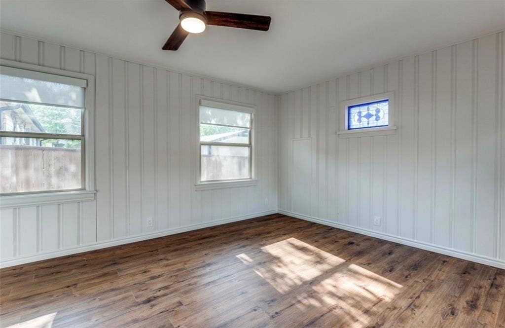 1323 Engle Avenue, Dallas, TX 75224 Wood-finish flooring, white vertical paneled walls, multiple windows, stained glass accent window, and a ceiling fan with integrated lighting