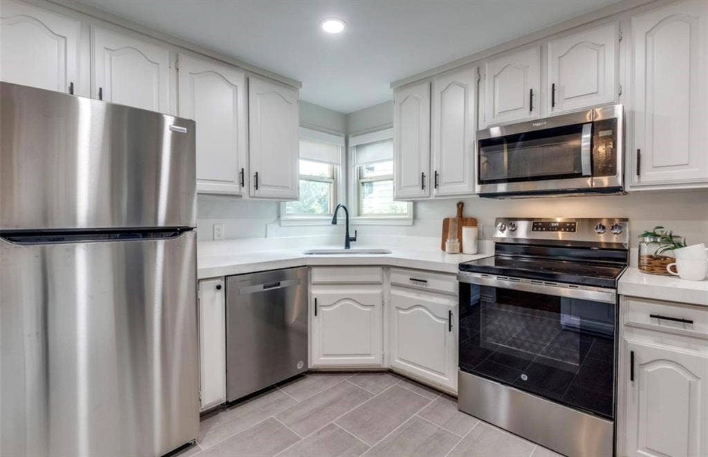 1323 Engle Avenue, Dallas, TX 75224 White cabinetry with black hardware, stainless steel appliances, light countertops, subway tile backsplash, and grey tile flooring