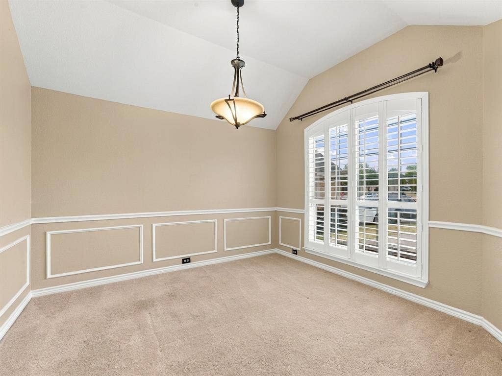 Vaulted ceiling with an attached light fixture, arched window with plantation shutters, wainscoting with decorative molding, and carpeting