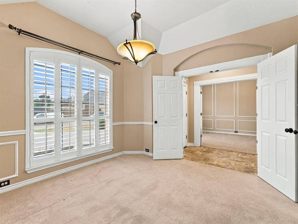 Arched window with plantation shutters, vaulted ceiling, and decorative molding