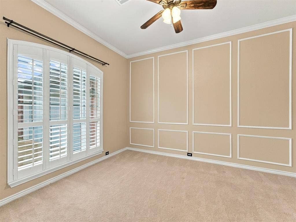 Arched window with plantation shutters, decorative wall molding, crown molding, ceiling fan with integrated lighting, and carpeted flooring