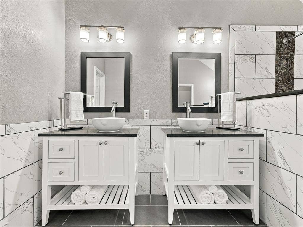 Dual white vanities with vessel sinks, dark countertops, and framed mirrors