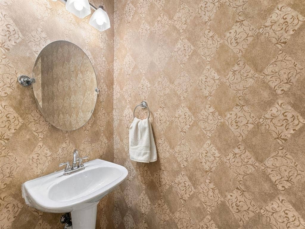 Pedestal sink with chrome faucet, oval wall-mounted mirror, and decorative wall covering