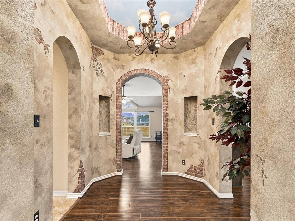 Arched doorways with brick detailing, recessed wall niches, wood-finish flooring, and an ornate chandelier