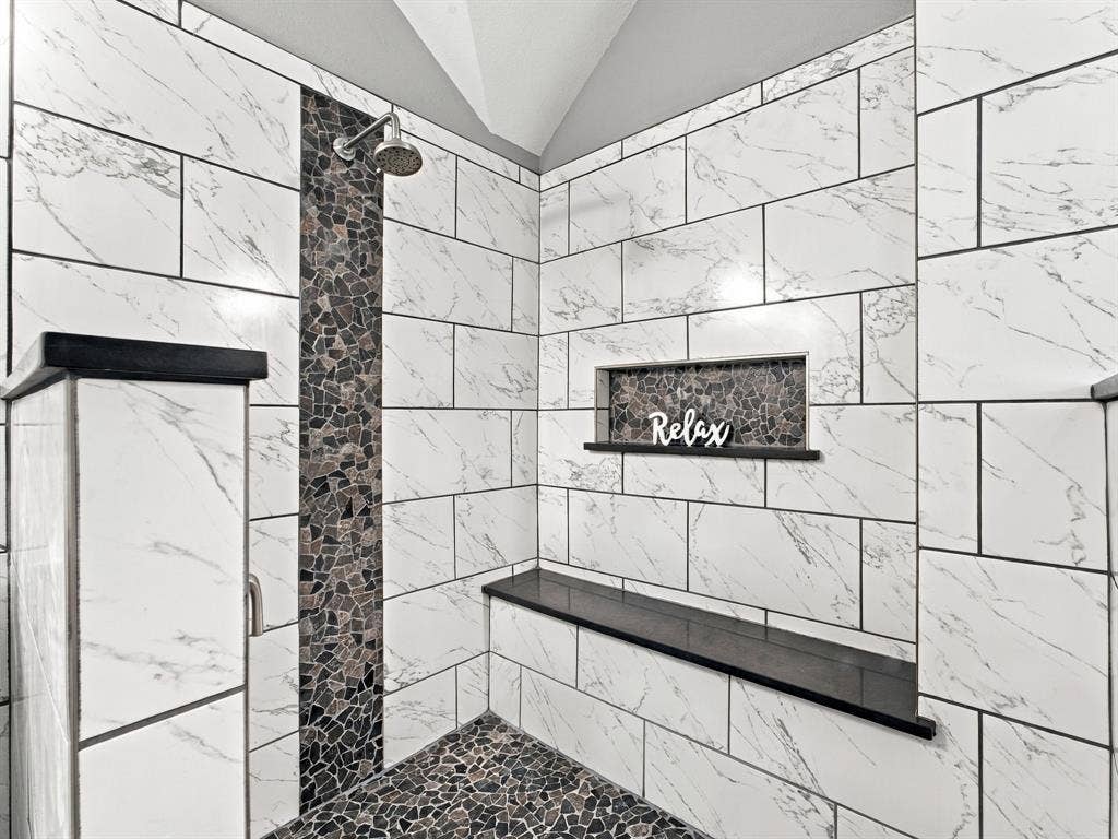 Spacious shower featuring white marble-look subway tile, a pebbled-tile floor, and a built-in shower niche