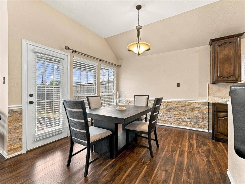 Vaulted ceiling with an attached light fixture, wood-finish flooring, stone-finish wainscoting, and a full-light exterior door