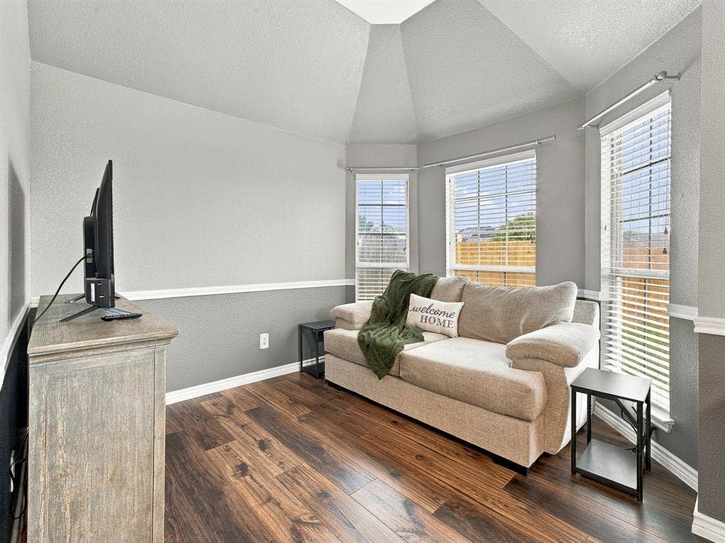 Wood-finish flooring with a two-tone wall treatment, vaulted ceiling, and multiple windows