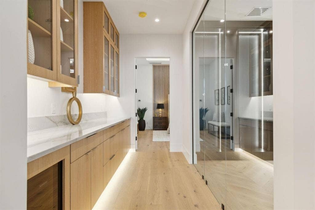 Large coffee bar just outside owners suite with beverage refrigerator, under cabinet lighting, stone countertops, and white oak flooring.