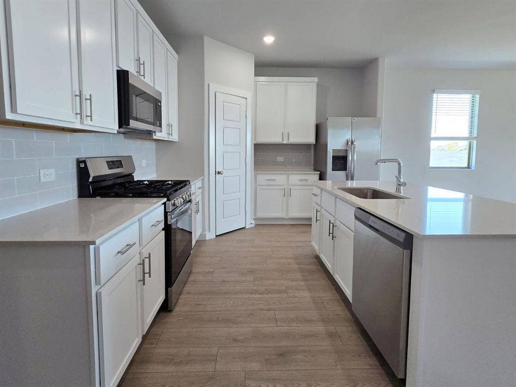 841 Rockcloud Drive, Fort Worth, TX 76052 Kitchen featuring wood-finish flooring, white cabinetry, integrated stainless steel appliances, light-toned countertops, and a subway tile backsplash