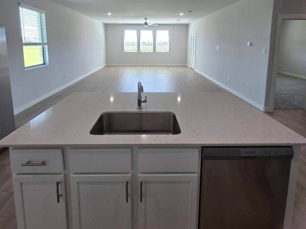 841 Rockcloud Drive, Fort Worth, TX 76052 Kitchen island featuring a stainless steel undermount sink, a chrome gooseneck faucet, light-toned countertop, and integrated dishwasher
