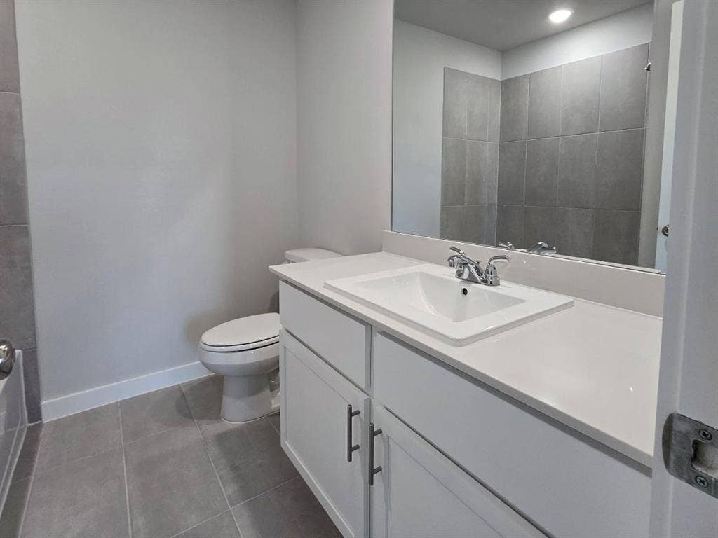 841 Rockcloud Drive, Fort Worth, TX 76052 Modern bathroom featuring a white vanity with an integrated sink, polished chrome faucet, rectangular mirror, and large format floor tiling