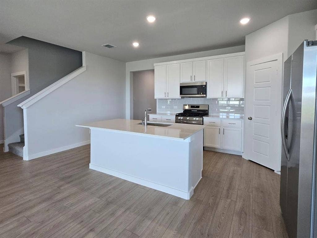 841 Rockcloud Drive, Fort Worth, TX 76052 Open-concept kitchen featuring white cabinetry, stainless steel appliances, a center island with sink, and wood-finish flooring
