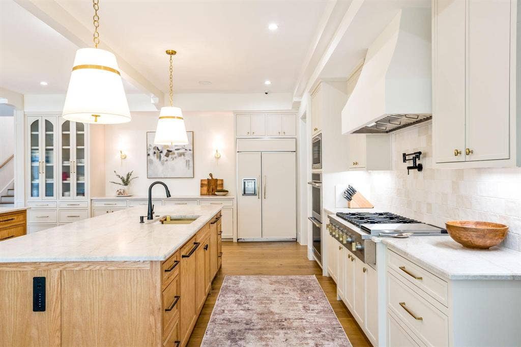 12007 Quincy Lane, Dallas, TX 75230 Gourmet kitchen featuring a large central island with a sink, built-in range, double wall ovens, and custom cabinetry