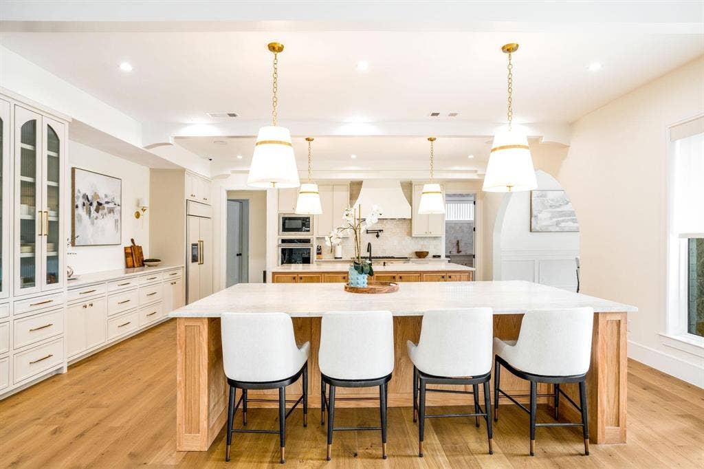 12007 Quincy Lane, Dallas, TX 75230 Wood-finish flooring, white cabinetry with gold-finish hardware, built-in double ovens, and a large kitchen island with seating