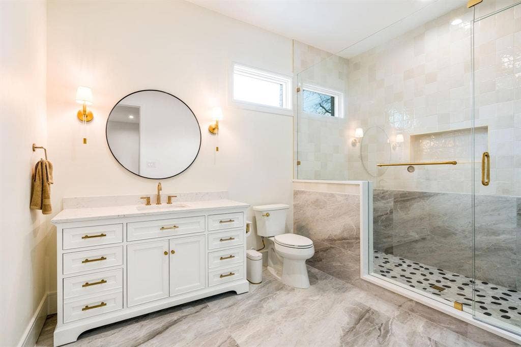 12007 Quincy Lane, Dallas, TX 75230 White vanity with gold-finish hardware and faucet, circular mirror, and two wall sconces