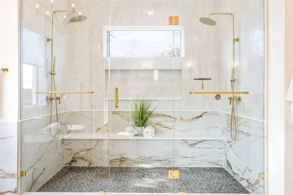 12007 Quincy Lane, Dallas, TX 75230 Dual rain shower heads with handheld sprayers, glass enclosure, built-in bench, marble-finish wall tiles, and pebble-tile flooring
