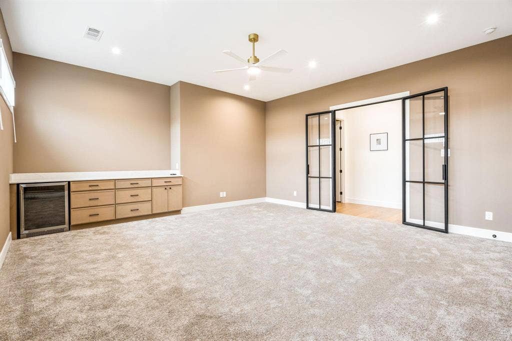 12007 Quincy Lane, Dallas, TX 75230 Built-in cabinetry with integrated beverage cooler, light-colored carpeting, recessed lighting, ceiling fan, and black-framed glass panel doors