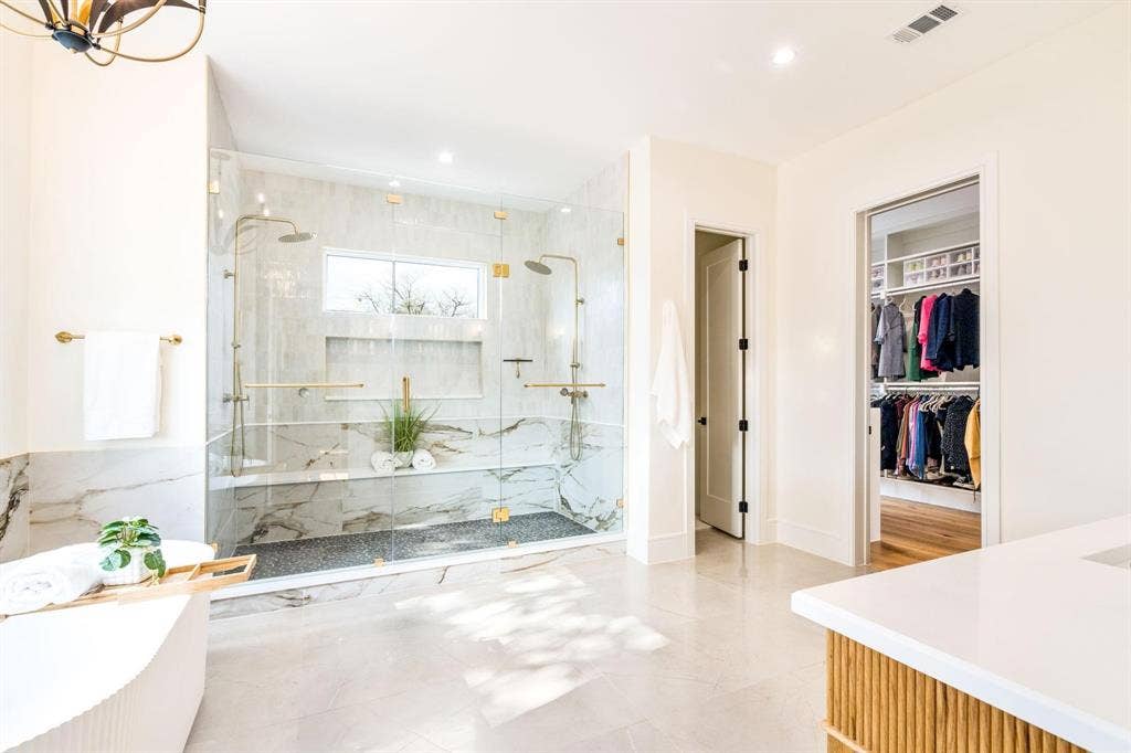 12007 Quincy Lane, Dallas, TX 75230 Spacious bathroom featuring a frameless glass shower enclosure, dual shower heads, a built-in shower bench, and a freestanding soaking tub