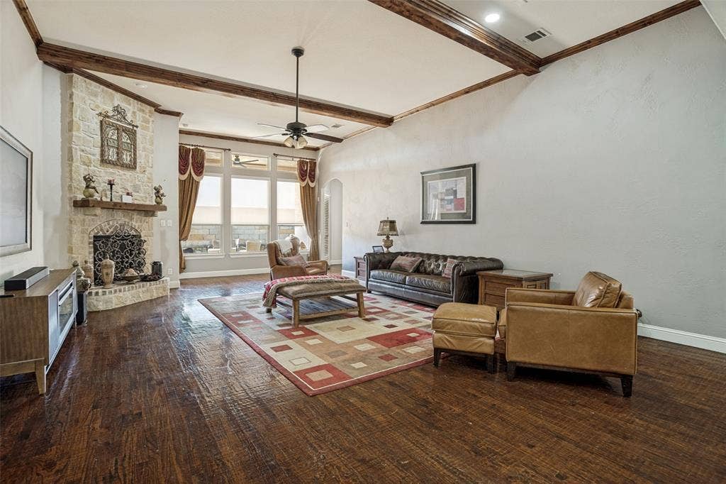 1250 Packsaddle Trail, Prosper, TX 75078 Vaulted ceiling with exposed wood beams, stone-clad fireplace with mantel, dark wood-finish flooring, and large windows