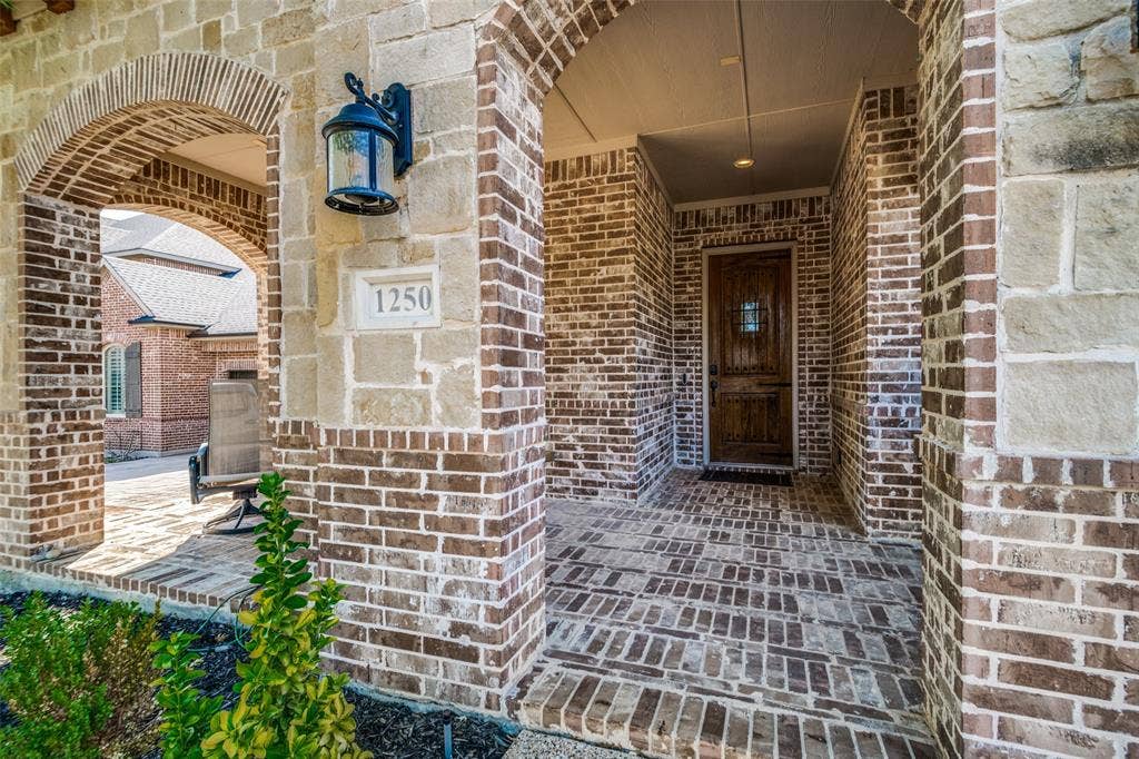 1250 Packsaddle Trail, Prosper, TX 75078 Arched brick entryway featuring a decorative wooden door with iron accents