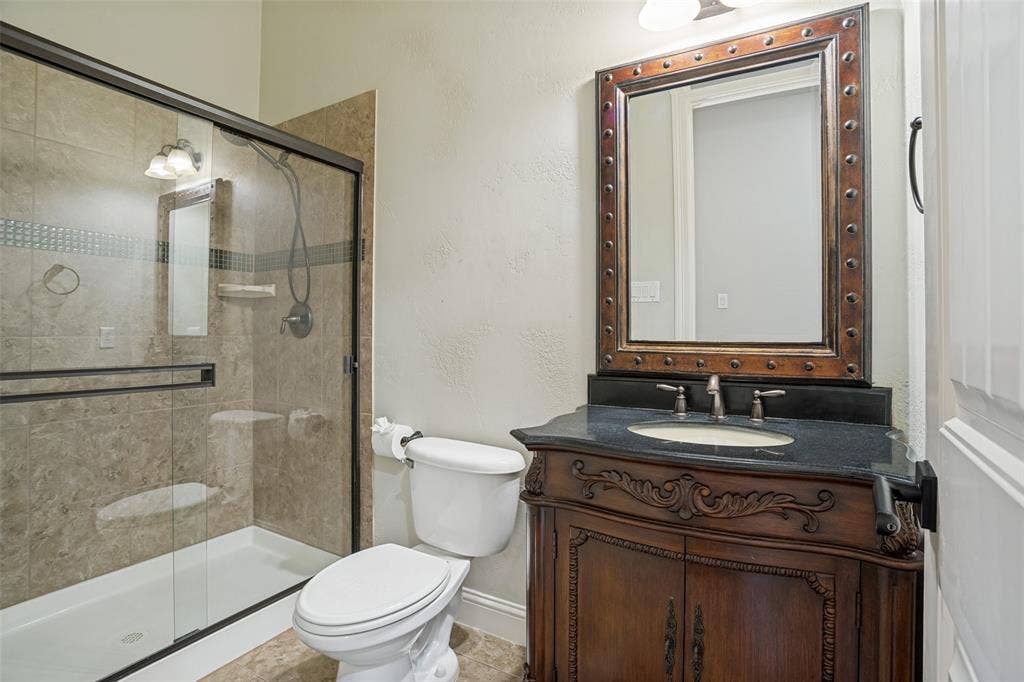 1250 Packsaddle Trail, Prosper, TX 75078 Frameless glass shower enclosure, decorative shower tile inlay, vanity with carved wood details, dark countertop, and decorative framed mirror