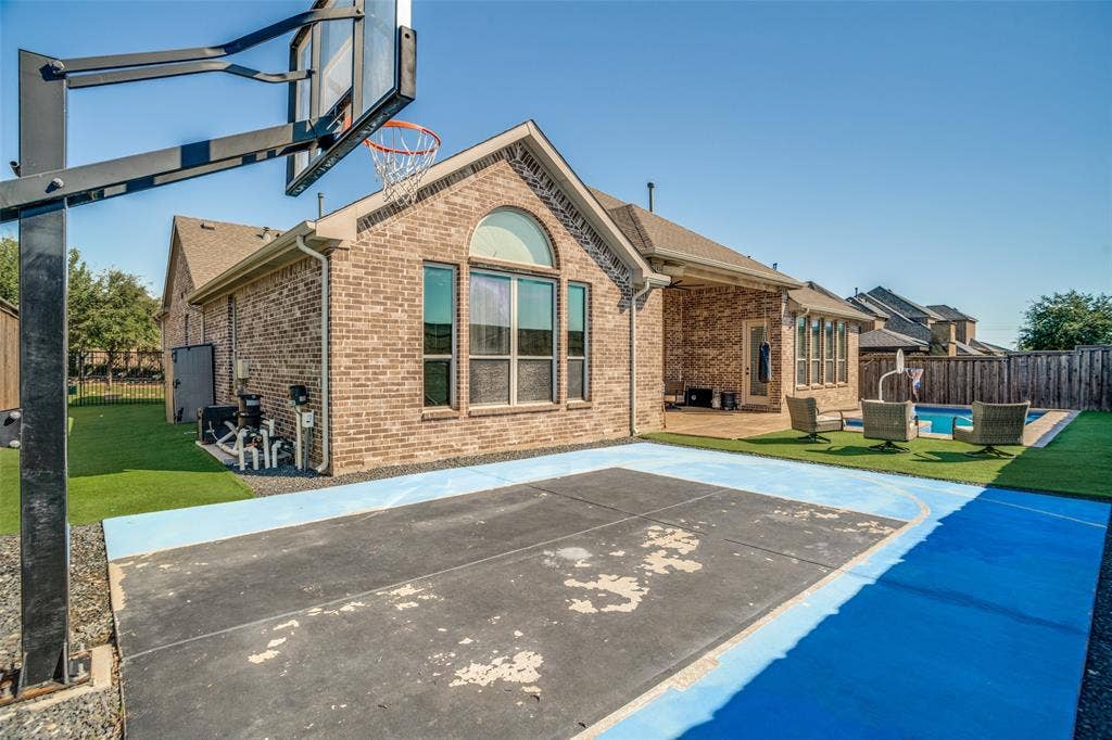 1250 Packsaddle Trail, Prosper, TX 75078 Brick exterior with arched windows, a covered patio, and a fenced backyard featuring a paved sports court, artificial turf, and an in-ground pool
