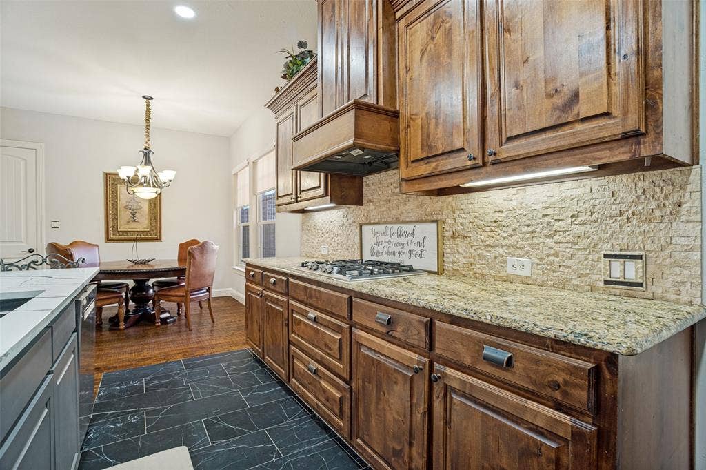 1250 Packsaddle Trail, Prosper, TX 75078 Kitchen with dark wood cabinetry, light-colored textured tile backsplash, and a built-in gas range